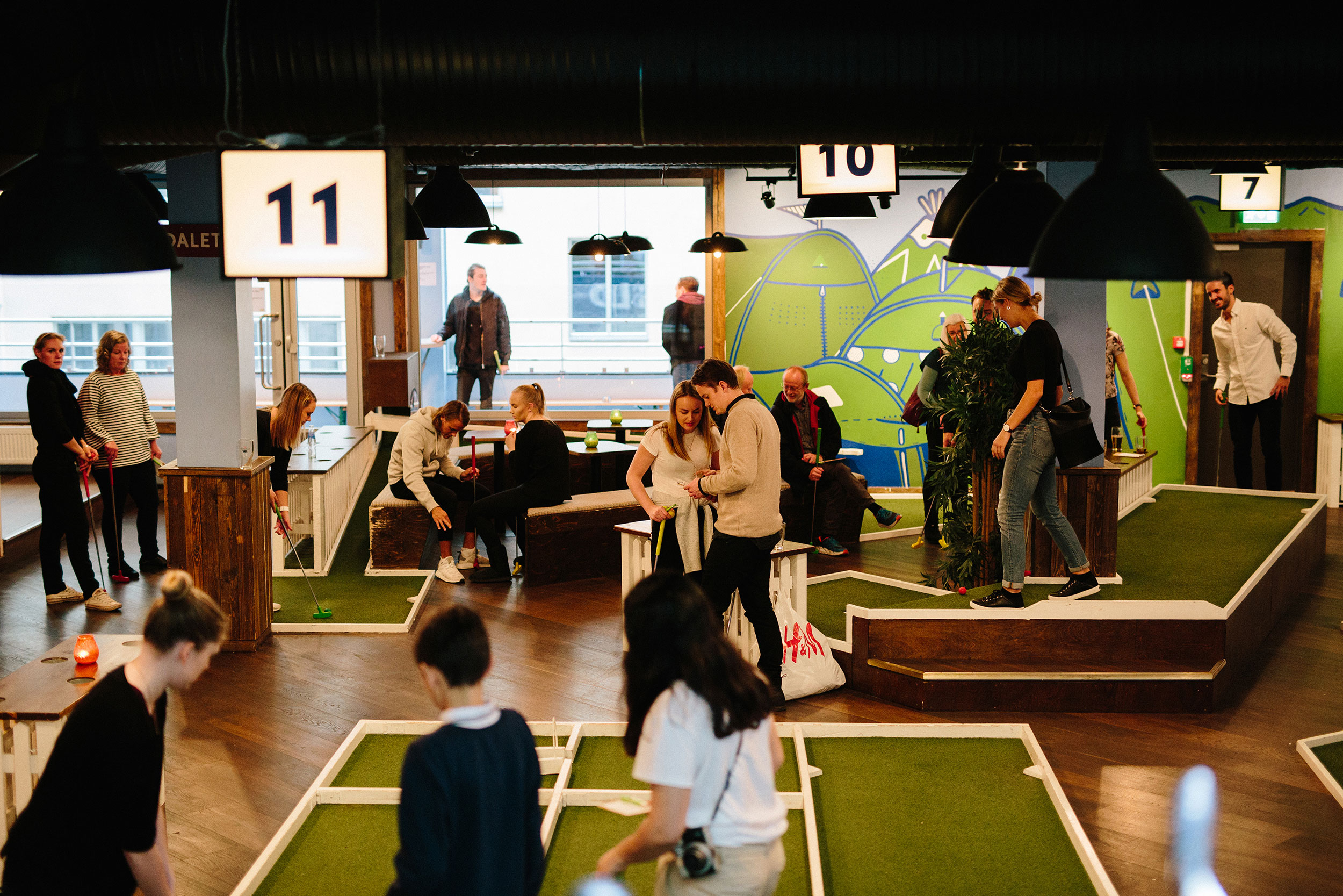Et titalls mennesker spiller minigolf på ulike baner innendørs