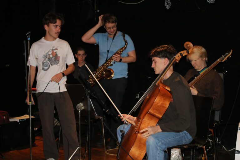 fem studenter med ulike instrumenter som cello og saxofon med mørk bakgrunn.