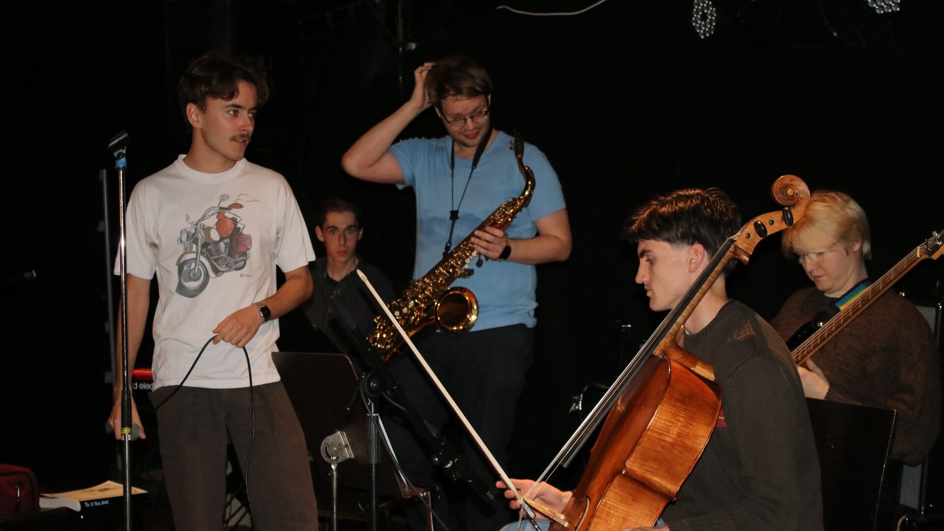 fem studenter med ulike instrumenter som cello og saxofon med mørk bakgrunn.
